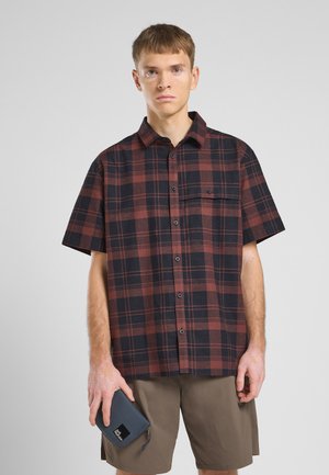 Chemise à manches courtes en tartan rouge foncé et bleu marine, avec un devant à boutons, une poche poitrine et une coupe décontractée. Associée à un short beige.