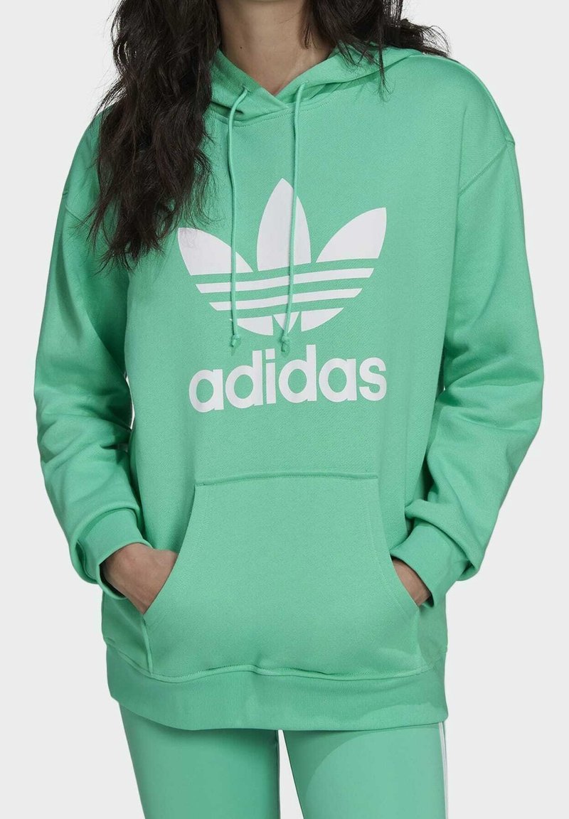 Grön huvtröja med en frontficka, dragsko i huvan och vitt Adidas-logotyp som har tre ränder och bladdesign. Mjuk tygstruktur.