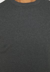 Gros plan d’une personne portant un pull en tricot côtelé gris foncé avec un col rond.