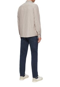 Beige knoopshirt met een gestructureerde afwerking, lange mouwen en twee plooien op de schouders aan de achterkant, gecombineerd met navy jeans en witte sneakers.