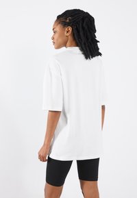 Hvid oversized t-shirt lavet af bomuld, med korte ærmer og rund udskæring. Bæres med sorte cykelshorts.