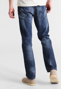 Blå denimjeans med rak passform, femfickorsdesign och minimal blekning, matchade med ljusa slip-on skor.