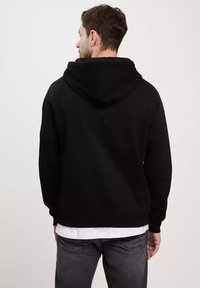 Czarna bluza z kapturem i sznurkiem, o miękkiej fakturze i prążkowanych mankietach. Nosi się ją na białej koszuli, zestawiona z szarymi dżinsami.