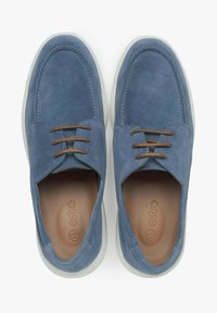 Blauwe suède schoenen met een afgeronde neus, bruine veters en witte rubberen zolen. Het interieur heeft een beige voering en een logo dat op de binnenzool is gedrukt.