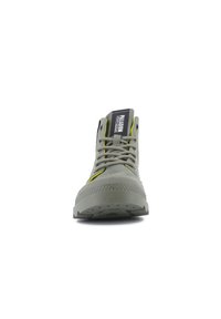 Grüner High-Top-Schuh aus Wildleder, mit runder Zehenpartie, gelben Akzenten, strukturiertem Gummisohle und auffälligem Logo auf der Zunge.