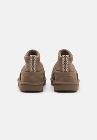 Bottines marron avec un dessus en daim, un col en tricot élastique et une semelle en caoutchouc. Présente une languette arrière texturée avec un motif en zigzag.