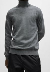 Grauer Rollkragenpullover aus weichem Strickmaterial, mit taillierter Passform und geripptem Kragen. Glatte Textur mit minimaler Detailgestaltung.