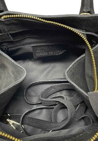 Interno di una borsa in suede nero con una zip dorata, due scomparti e un'etichetta che dice "Made in Italy." Presenta un tessuto testurizzato e manici.
