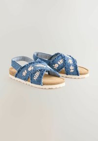 Sandali in denim con cinturini incrociati e ricamo floreale bianco, soletta imbottita beige e suola in gomma bianca testurizzata.