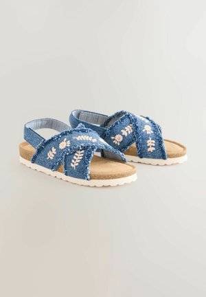 Sandalias vaqueras con tiras cruzadas y bordado floral blanco, plantilla acolchada en color beige y suela de goma texturizada blanca.