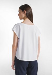 Top blanco de manga corta con un ajuste holgado. Presenta un escote amplio y una pequeña etiqueta en el centro de la parte trasera. La tela parece suave y lisa.