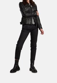 Svart bikerjacka i läder med dragkedjedetaljer, grå lager-på-lager-topp under, kombinerat med svarta slim-fit jeans och robusta svarta ankelboots.