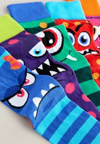 Calcetines novedosos y coloridos con caras de monstruos de dibujos animados, diversos patrones y texturas. Los colores incluyen azul, verde, morado y naranja.