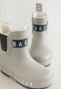 Grijze rubberen laarzen hebben een zachte, witte voering, zwarte accenten met 'BAKER' branding en een gestructureerde zwarte zool voor grip.