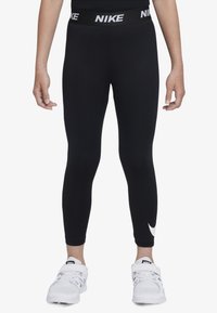 Mustat Nike-legginssit, joissa on leveä vyötärönauha ja valkoinen "NIKE"-teksti. Nilkan lähellä on pieni valkoinen Swoosh-logo. Tasainen kangaspinta.