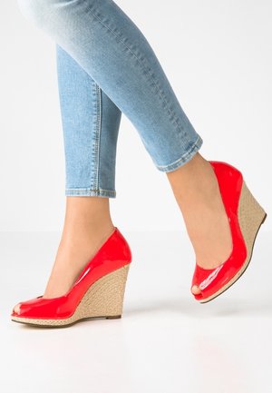 Czerwone lakierowane koturny na obcasie z odkrytym noskiem, z plecioną juty podeszwą i połyskującym wykończeniem. Połączone z dopasowanymi jasnoniebieskimi jeansami.