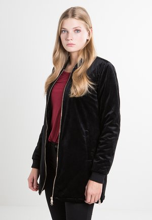 Mustmust bomber-jakk musta sametist, millel on esitasku, küljetaskud ja soonikud. Kantud marooni värvi sisaesemel, omab sileda tekstuuriga viimistlust.