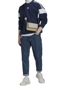 Mörkblå sweatshirt med vita ränder, löst sittande jeans i denim, vita sneakers och en beige axelremsväska med dragkedja.