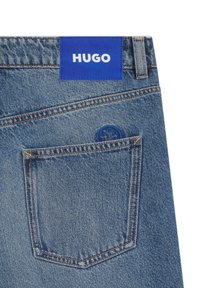 Jeans en denim bleu clair avec une étiquette bleue sur laquelle figure "HUGO" en blanc. Comprend une poche arrière avec un logo bleu circulaire.