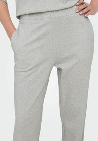 Lichtgrijze zachte stoffen broek met elastische tailleband, handen in de zakken, gedragen met bijpassend topje zichtbaar bij de taille.