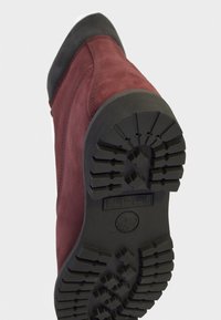 Bordeaux-farbene Wildleder-Stiefelette mit einer schwarzen Gummisohle. Die Sohle hat ein strukturiertesprofil für Grip und Stabilität.