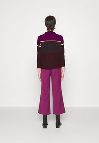 Brede trui van gebreid materiaal met kleurblokken in paars, bruin en geel; gecombineerd met wijde paarse broek. Zachte textuur; getailleerde silhouet.