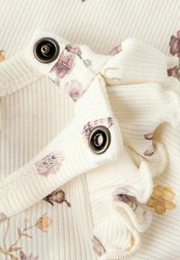 Zbliżenie na biały materiał z kwiatowymi wzorami, z falbankami i guzikami, ukazujące delikatne detale i tekstury.