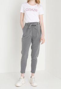 Grijze tapers met een strikdetail in de taille, gecombineerd met een witte T-shirt met rode tekst, en stevige witte sneakers.