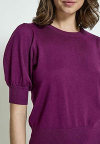 Lila Strickpullover mit kurzen Puffärmeln sowie einem gerippten Halsausschnitt und Saum, der eine weiche Textur und eine taillierte Silhouette aufweist.