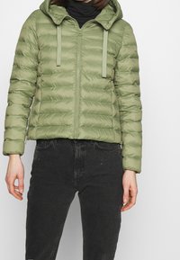Olivengrøn puffjakke med en tætsiddende design, lynlås lukning, elastiske manchetter og hætte. Glat, let materiale med sydde paneler.