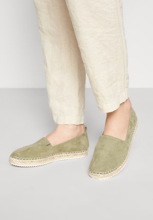 Grønne ruskinds espadriller med en jutesål og stikninger, der har lukket tå og sider, parret med beige linnedbukser.