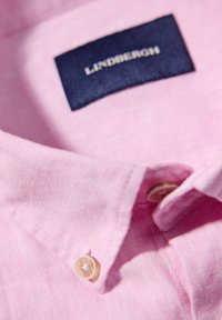 Lichtroze linnen overhemd met een marineblauwe label, met een puntkraag en een knoopdetail nabij de kraag. De textuur lijkt zacht en ademend.