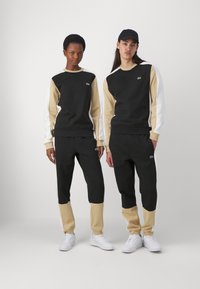 Completo attivo nero e beige con design a blocchi di colore. I felpe hanno polsini a costine; i pantaloni presentano caviglie elasticizzate; dettaglio del logo sul petto.