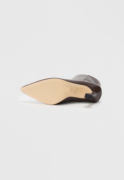 Stivale alla caviglia in pelle marrone scuro con punta affusolata, sdraiato su un lato, che mostra la suola liscia color cuoio e il piccolo tacco nero.