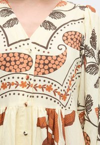 Φόρεμα με V ντεκολτέ και κουμπιά, με καφέ και πορτοκαλί floral και αφηρημένα μοτίβα σε κρεμ ύφασμα και φουσκωτά μανίκια.