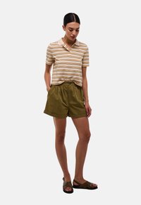 Polo-shirt à rayures, à manches courtes, en beige, orange et vert ; short ample vert olive ; sandales brunes à lanières. Design minimaliste, coupe décontractée.