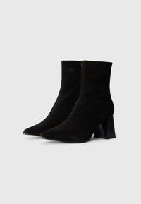 Bottines en daim noir avec un bout pointu, une fermeture éclair sur le côté et un talon large. Texture lisse sans motifs visibles.