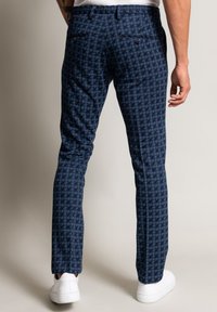 Kalhoty na míru s tmavě modrým vzorem psího zubu. Mají dvě zadní kapsy, rovný přední díl a úzký střih. Kombinovány s bílými teniskami.