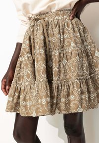 Jupe en tissu marron à volants ornée de motifs floraux et paisley blancs. Elle possède une taille élastique avec un cordon de serrage.