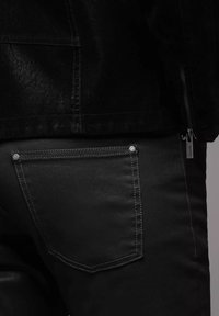 Pantalones de cuero sintético negros con un bolsillo trasero con remaches plateados. La textura suave y las costuras en contraste acentúan el diseño.