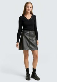 Black long-sleeve top with lace trim at the neckline, paired with a black faux leather A-line skirt. Model wearing black socks and platform shoes.