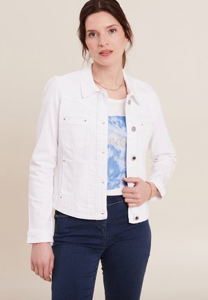 Weiße Jeansjacke mit einem klassischen Kragen, vorderen Taschen und silbernen Beschlägen. Über einem blauen Batikoberteil getragen und mit dunklen Jeans kombiniert.