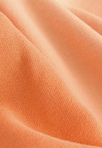 Tejido suave y texturizado en color durazno, que presenta una superficie lisa y un patrón de punto fino con sutiles variaciones en el tono.