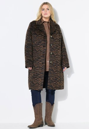 Cappotto di lana marrone e nero a strisce zebrate, con un ampio colletto e chiusura a bottoni, abbinato a una camicia di pelle marrone, jeans e stivali da cowboy.