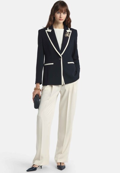 Námornícka modrá bunda s bielym kontrastným lemovaním, zapínanie na jeden gombík, v páre s krémovými širokými nohavicami a čiernymi špicatými podpätkami. S logom.