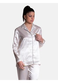 Pigiama in satin bianco morbido con piping nero. La camicia presenta una chiusura con bottoni e colletto a punta. Tessuto liscio e vestibilità comoda.