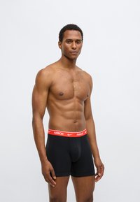 Fekete boxeralsó piros Nike logós derékpánttal. Az anyaga simának tűnik, testhezálló kialakítású, normál hosszúságú és varrásokkal ellátott.