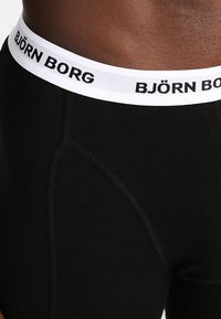 Čierne bavlnené boxerky majú biely elastický pás s čiernym nápisom "BJÖRN BORG". Dizajn obsahuje viditeľné švy a kontúry.