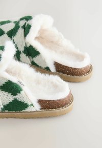 Zielono-białe, w kratkę, dzianinowe kapcie z puszystym białym wykończeniem i brązowym korkowym akcentem. Gumowa podeszwa dla lepszej przyczepności.