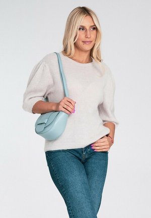 Jasnobeżowy sweter z bufkami na rękawach, zestawiony z niebieskimi dżinsami. Mała jasnoniebieska skórzana torebka na ramię z klapką.